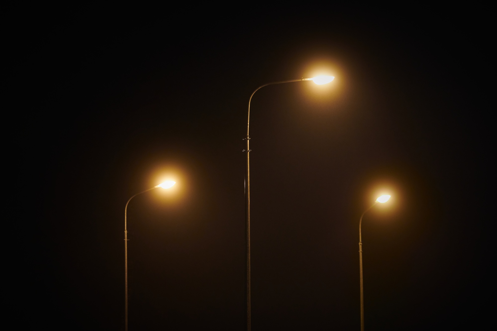 Three night lamppost shines with faint mysterious yellow light through evening fog at quiet night